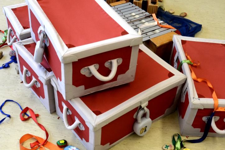 Schulprojekt "Hospiz macht Schule" Bunte Kisten mit roten Oberflächen, umgeben von bunten Bändern und Spielzeugen.