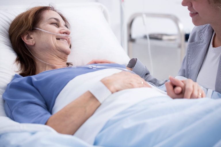 Ambulanter Hospiz- und Palliativberatungsdienst Lächelnde Patientin im Krankenhausbett, umgeben von einer unterstützenden Person.